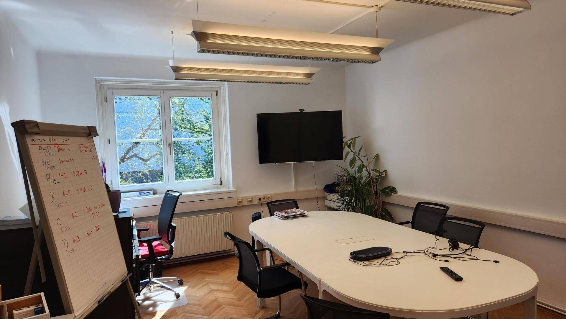 Modern eingerichtetes Büro mit großem Konferenztisch, Parkettboden und Tageslicht.