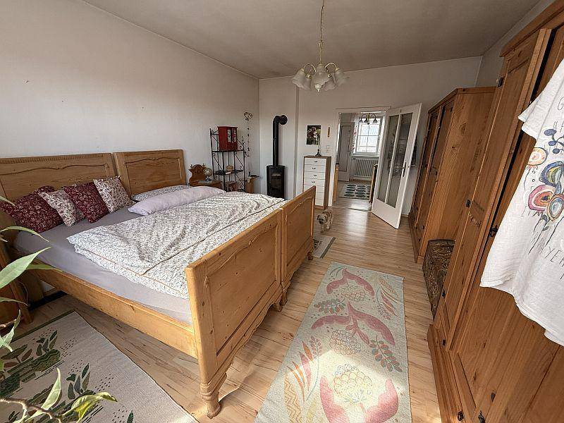 Helles Schlafzimmer mit Holzboden, Doppelbett, Holzschränken und einem Holzofen.