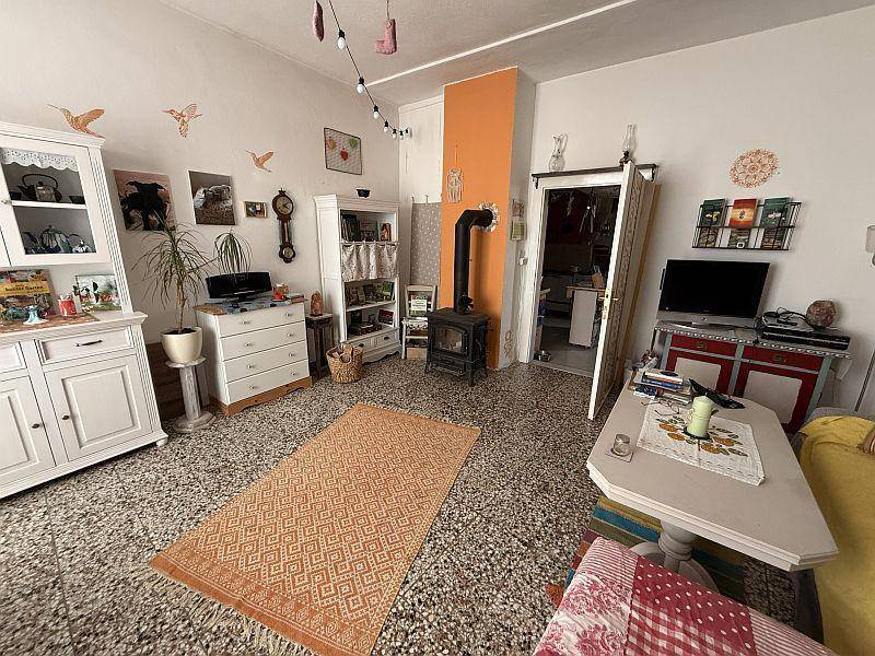 Helles Wohnzimmer mit Terrazzoboden, Holzofen und traditionellen Möbeln.