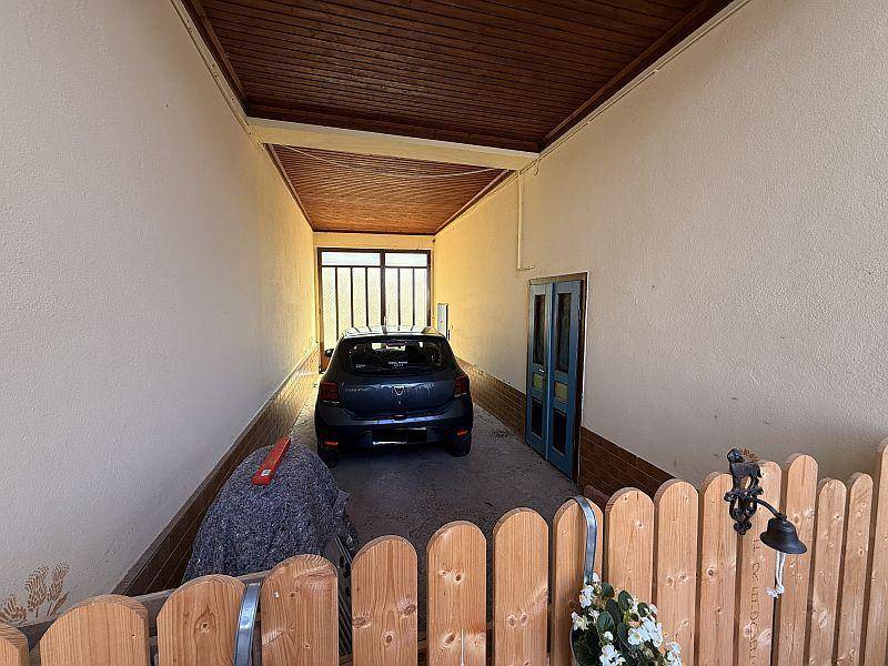 Überdachter Stellplatz für ein Fahrzeug mit Holzzaun und Zugang zum Haus.