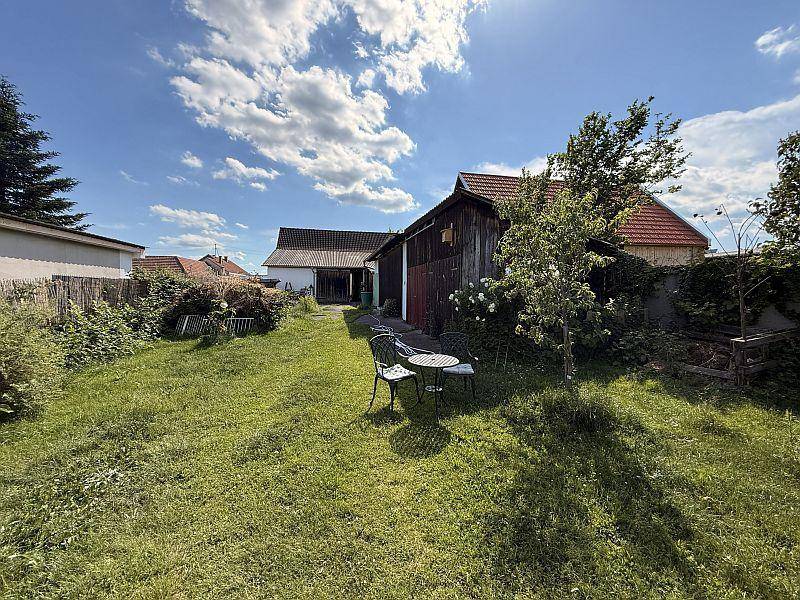 Großer, sonniger Garten mit Rasenfläche, alten Schuppen und Sitzgelegenheiten im Freien.