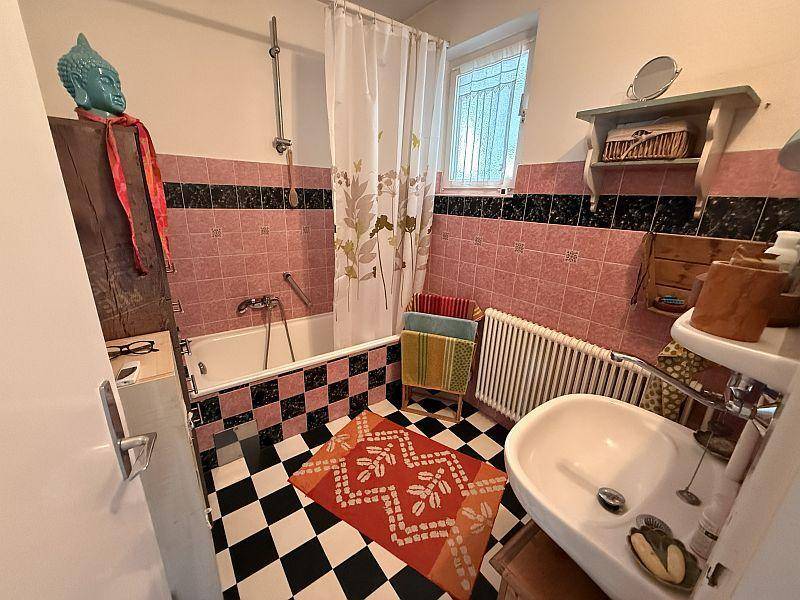 Badezimmer mit Badewanne, Waschbecken, rosa Fliesen und schwarz-weißem Schachbrettboden.