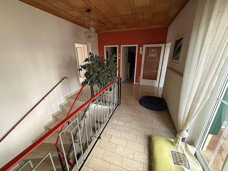 Heller Flur mit Treppe, Fliesenboden und einem großen Fenster.