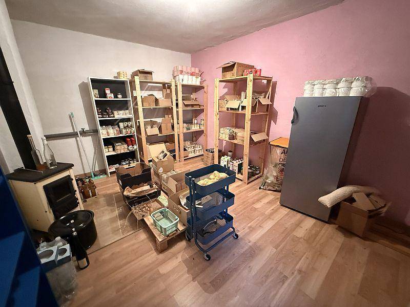 Lagerraum mit Regalen voller Vorräte, einem Kühlschrank und rosa gestrichenen Wänden.