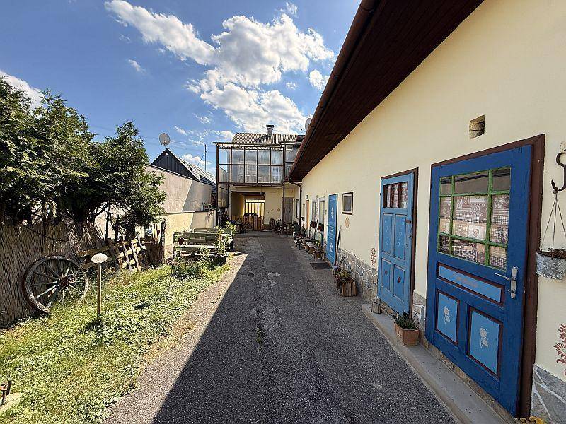 Sonniger Außenbereich mit einem gepflasterten Weg, blauen Türen und einem kleinen Gartenbereich.