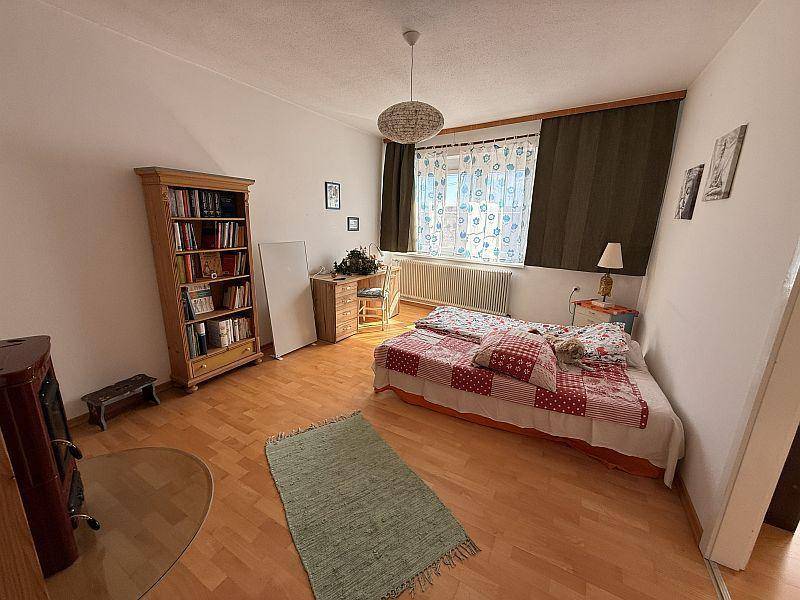 Gemütliches Schlafzimmer mit Holzboden, Holzofen und einem Doppelbett mit karierter Decke.