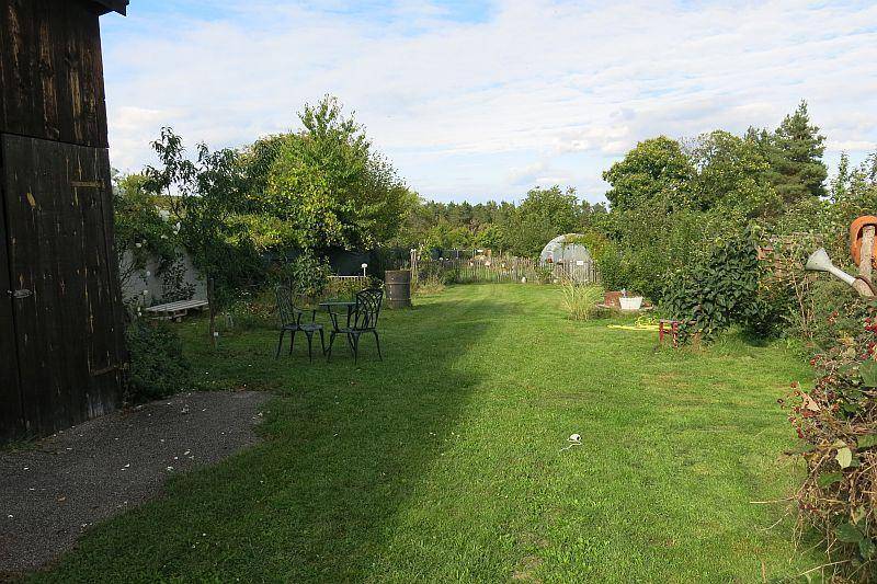 Großer Garten mit weitläufiger Rasenfläche, Bäumen und einer kleinen Sitzgruppe, ideal für Outdoor-Aktivitäten.