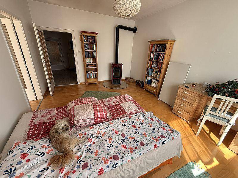 Schlafzimmer mit Holzboden, Holzofen und einem Doppelbett mit floraler Bettwäsche.