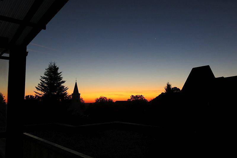 Malerischer Sonnenuntergang über einer Silhouette von Bäumen und einem Kirchturm, der den Himmel färbt.