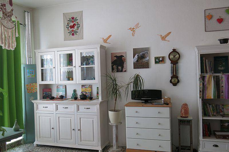 Gemütliches Wohnzimmer mit weißen Schränken, Pflanzen und persönlichen Dekorationen, die eine wohnliche Atmosphäre schaffen.