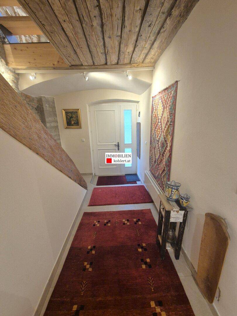 Eingangsbereich mit Holzbalkendecke, Fliesenboden und Teppichen, der zur Haustür führt.