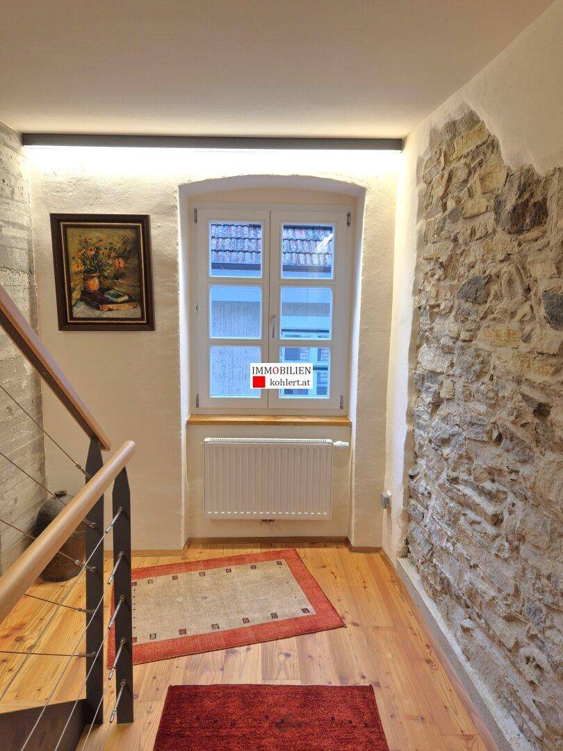 Heller Treppenabsatz mit Holzdielenboden, Fenster und freiliegender Steinwand.