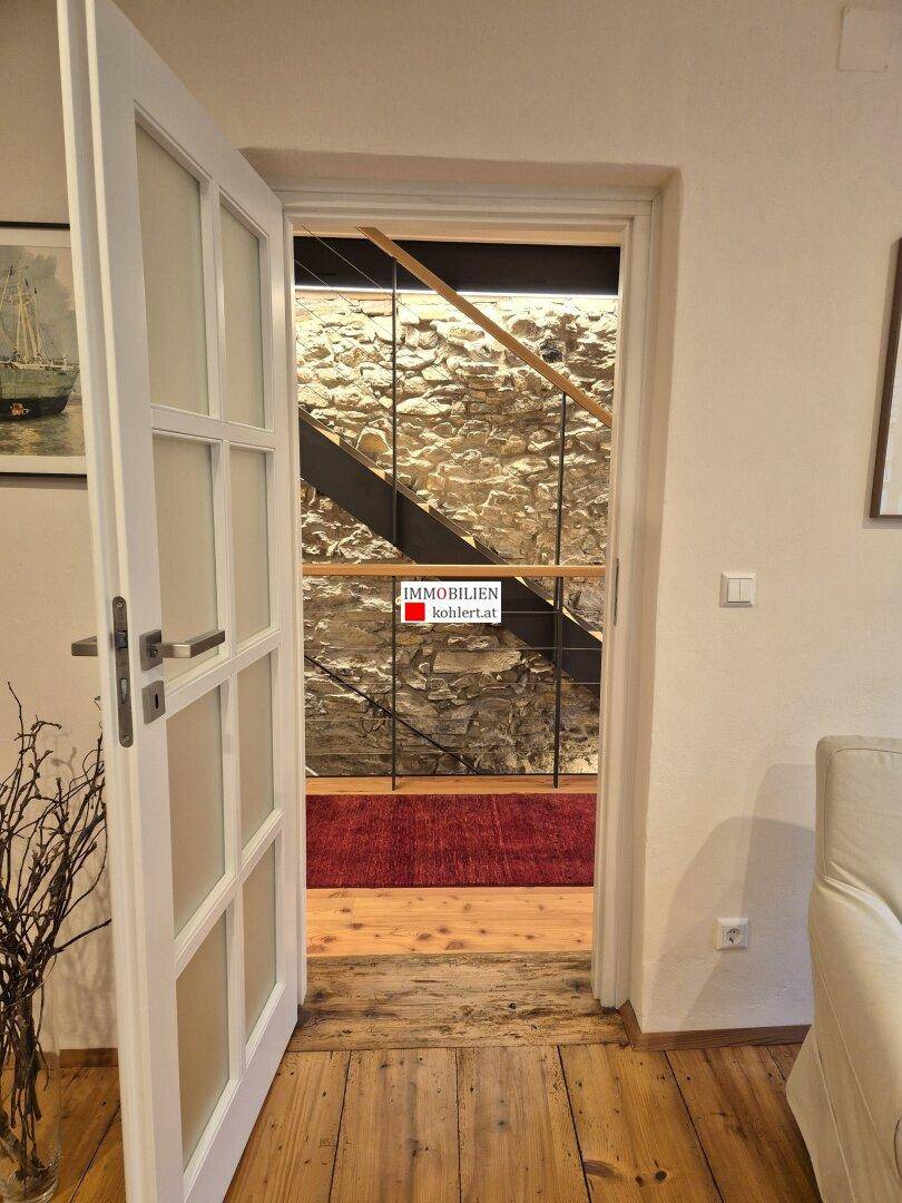 Blick durch eine offene Tür auf eine moderne Treppe mit Steinwand und Holzfußboden.
