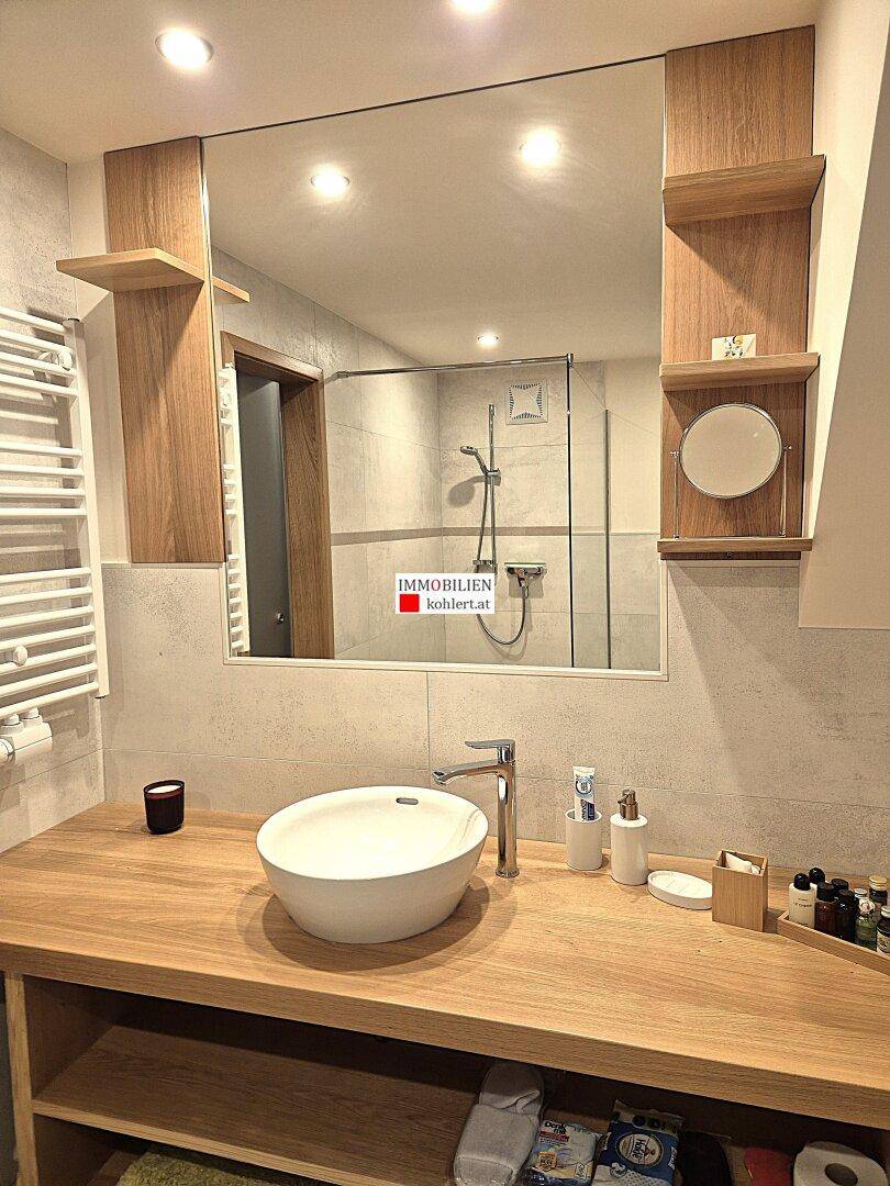 Modernes Badezimmer mit Aufsatzwaschbecken, Holzwaschtisch und großer Spiegelfläche.
