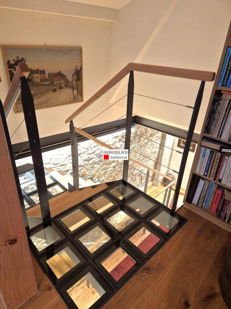 Oberer Treppenbereich mit Holzdielenboden, Glasboden und Bücherregal.