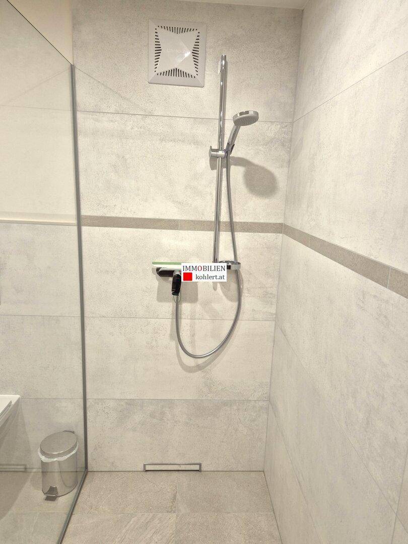 Duschbereich in einem modernen Badezimmer mit großformatigen Fliesen und Regenbrause.