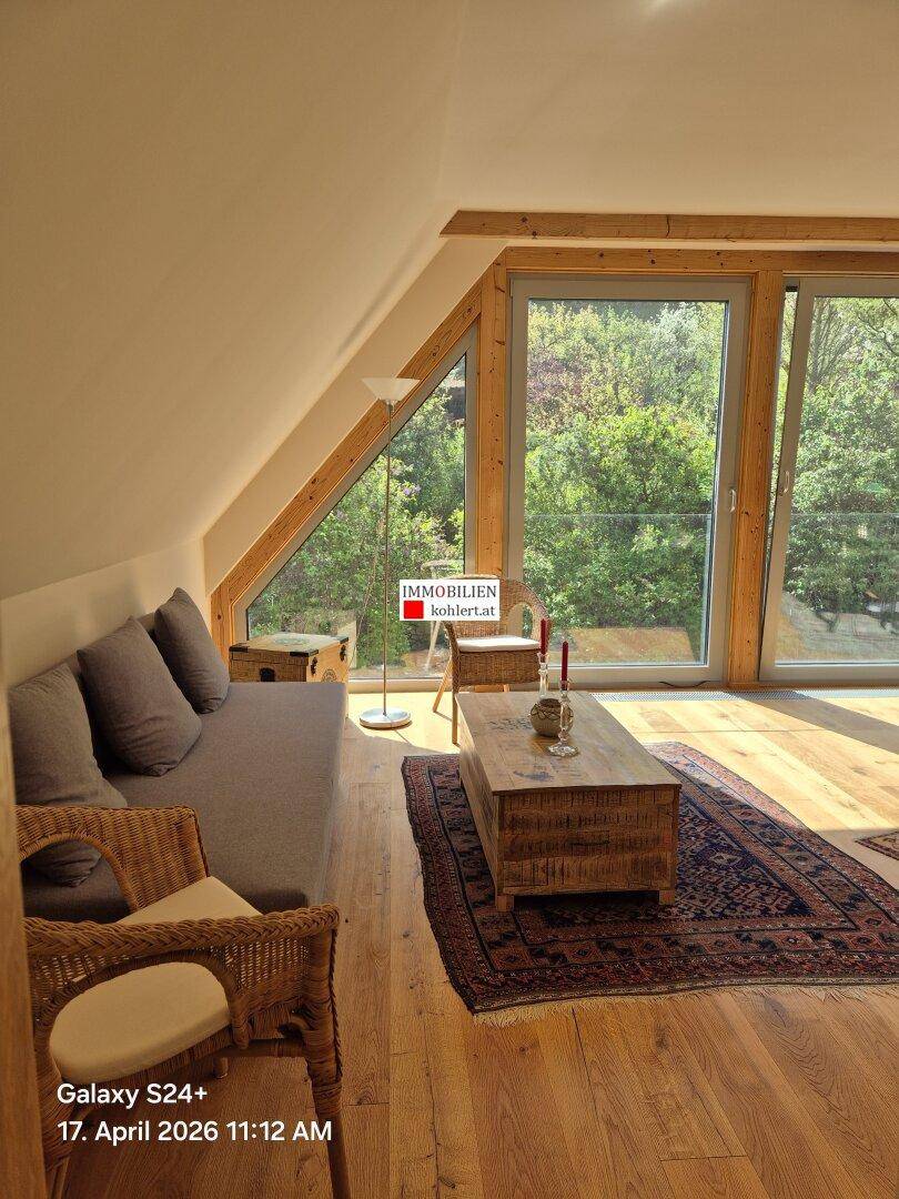 Helles Wohnzimmer im Dachgeschoss mit großen Fenstern, Holzbalken und Blick ins Grüne.