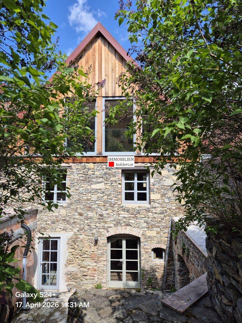 Historisches Gebäude mit Steinfassade, Holzelementen und grüner Umgebung.