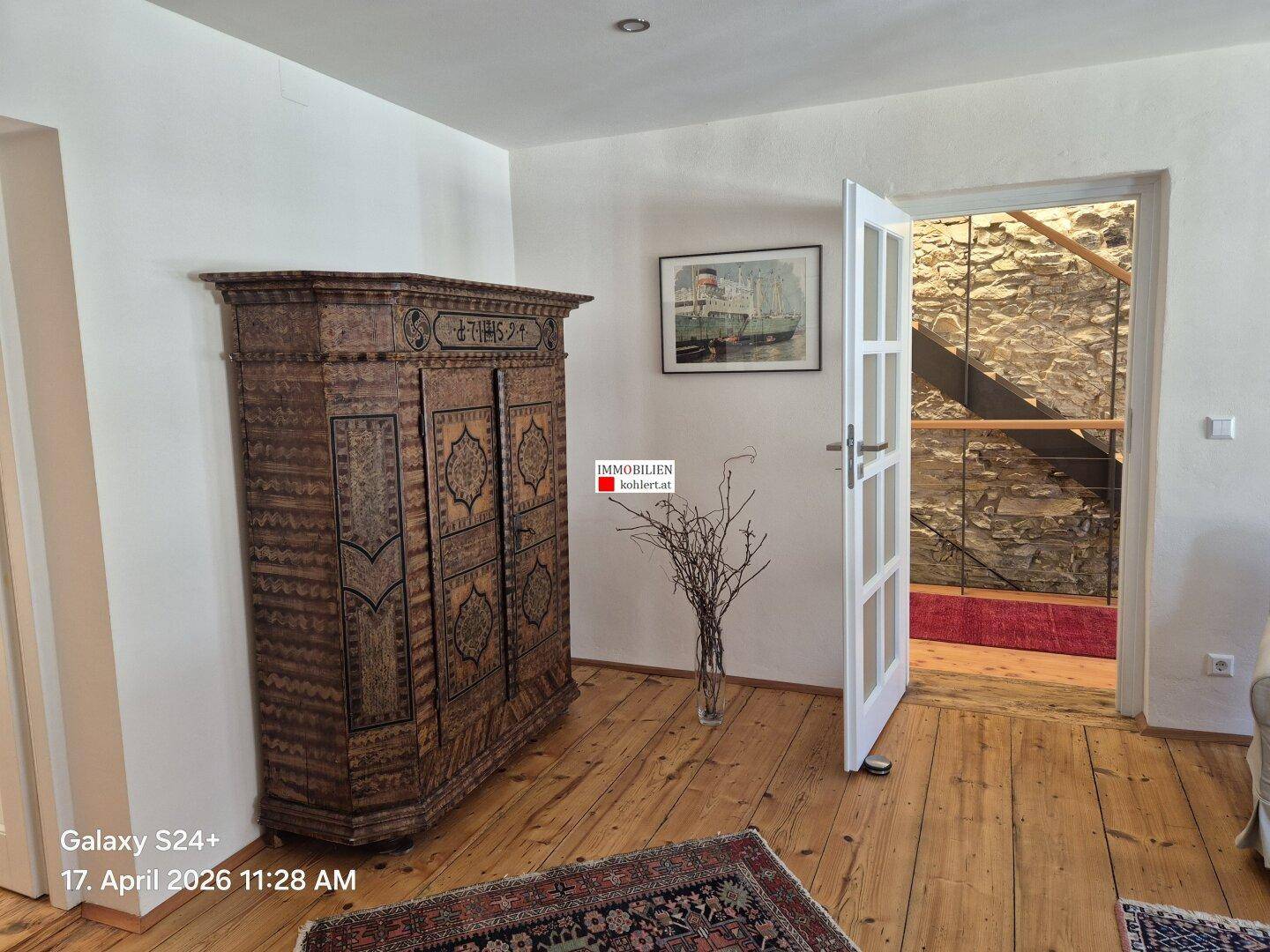 Wohnzimmer mit antikem Holzschrank, Holzdielenboden und Blick auf die Treppe.