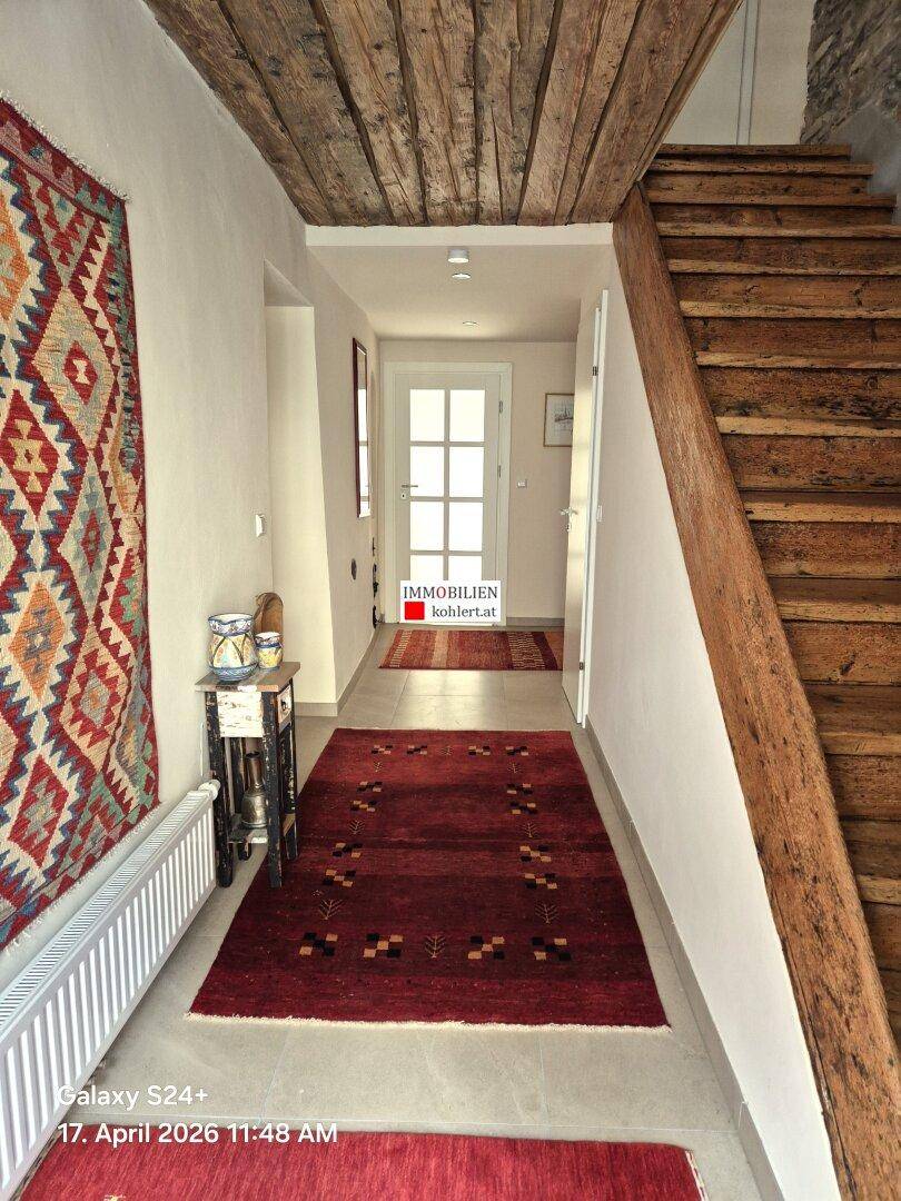 Flur mit Holztreppe, Holzbalkendecke und Fliesenboden, der zu den oberen Etagen führt.