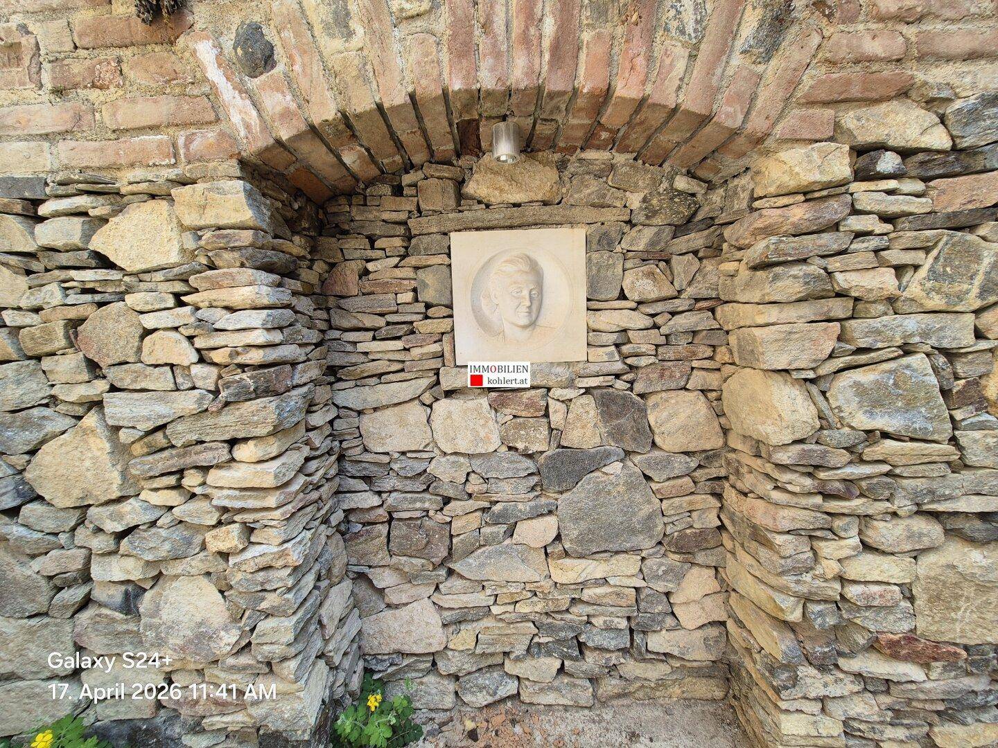 Historische Steinfassade mit Nische und einem Relief, umgeben von Naturstein.