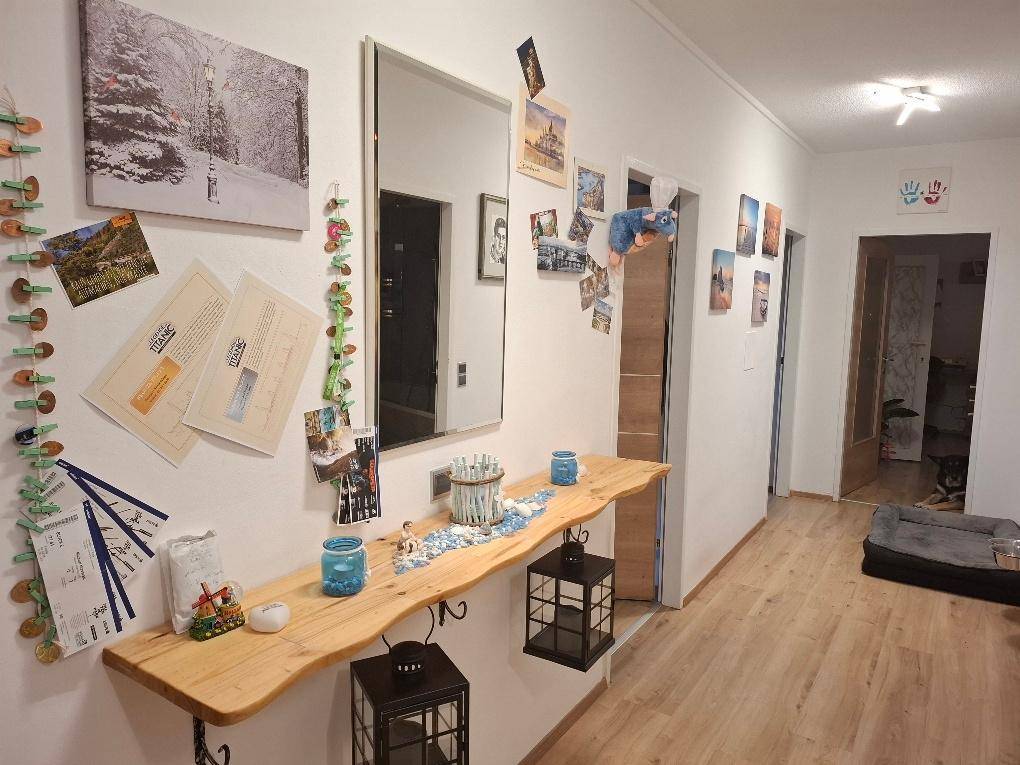 Heller Flur mit einer rustikalen Holzkonsole, großem Spiegel und persönlichen Dekorationen auf Holzfußboden.
