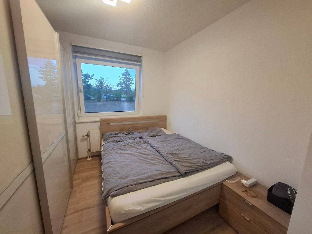 Schlafzimmer mit Doppelbett, Nachttisch, Kleiderschrank und einem Fenster, das Tageslicht hereinlässt.