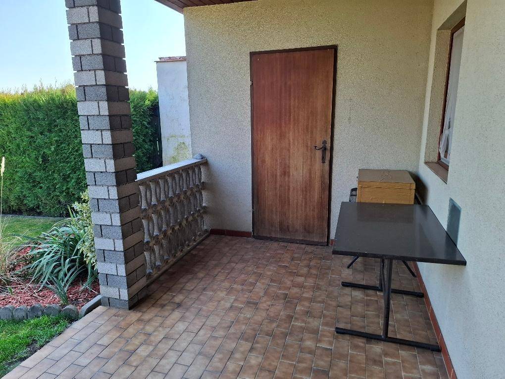 Überdachte Terrasse mit Fliesenboden, gemauertem Pfeiler und Zugang zum Garten.