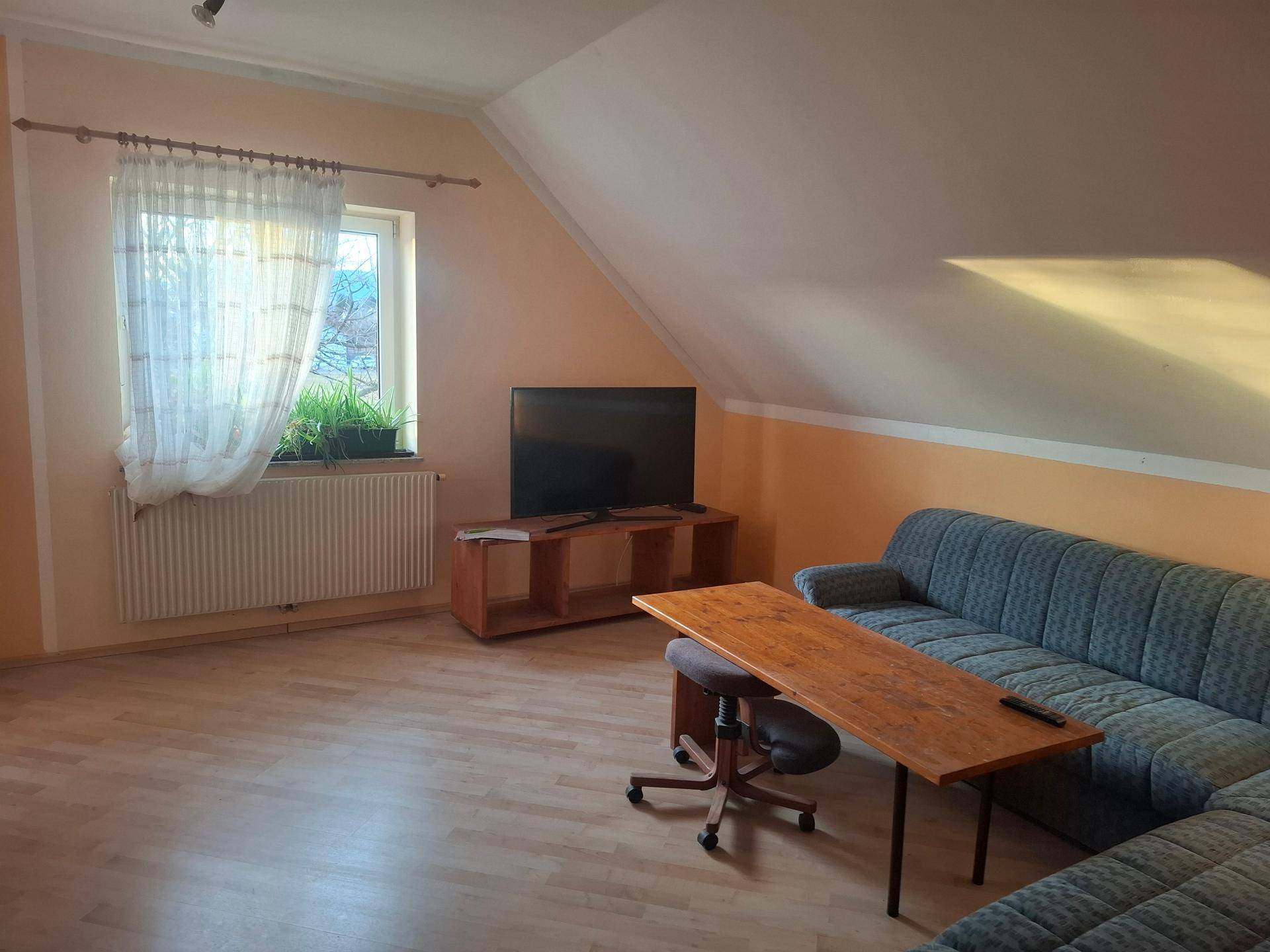 Gemütliches Wohnzimmer im Dachgeschoss mit Schrägen, Laminatboden und Sofa.