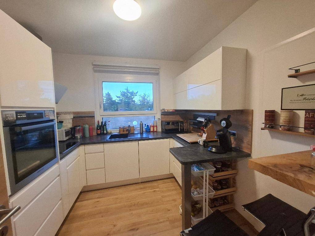 Moderne Küche mit weißen Hochglanzschränken, dunkler Arbeitsplatte, Einbauofen und einem Fenster mit Ausblick.