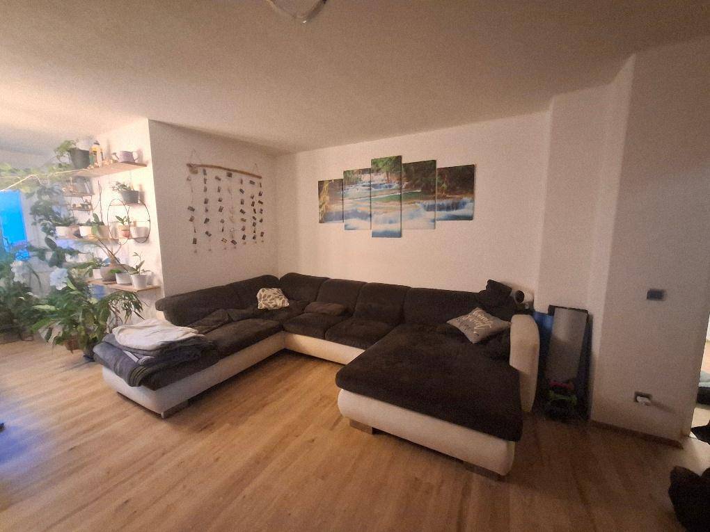 Geräumiges Wohnzimmer mit großem Ecksofa, Holzfußboden und dekorativen Wandbildern, die eine Wasserlandschaft zeigen.