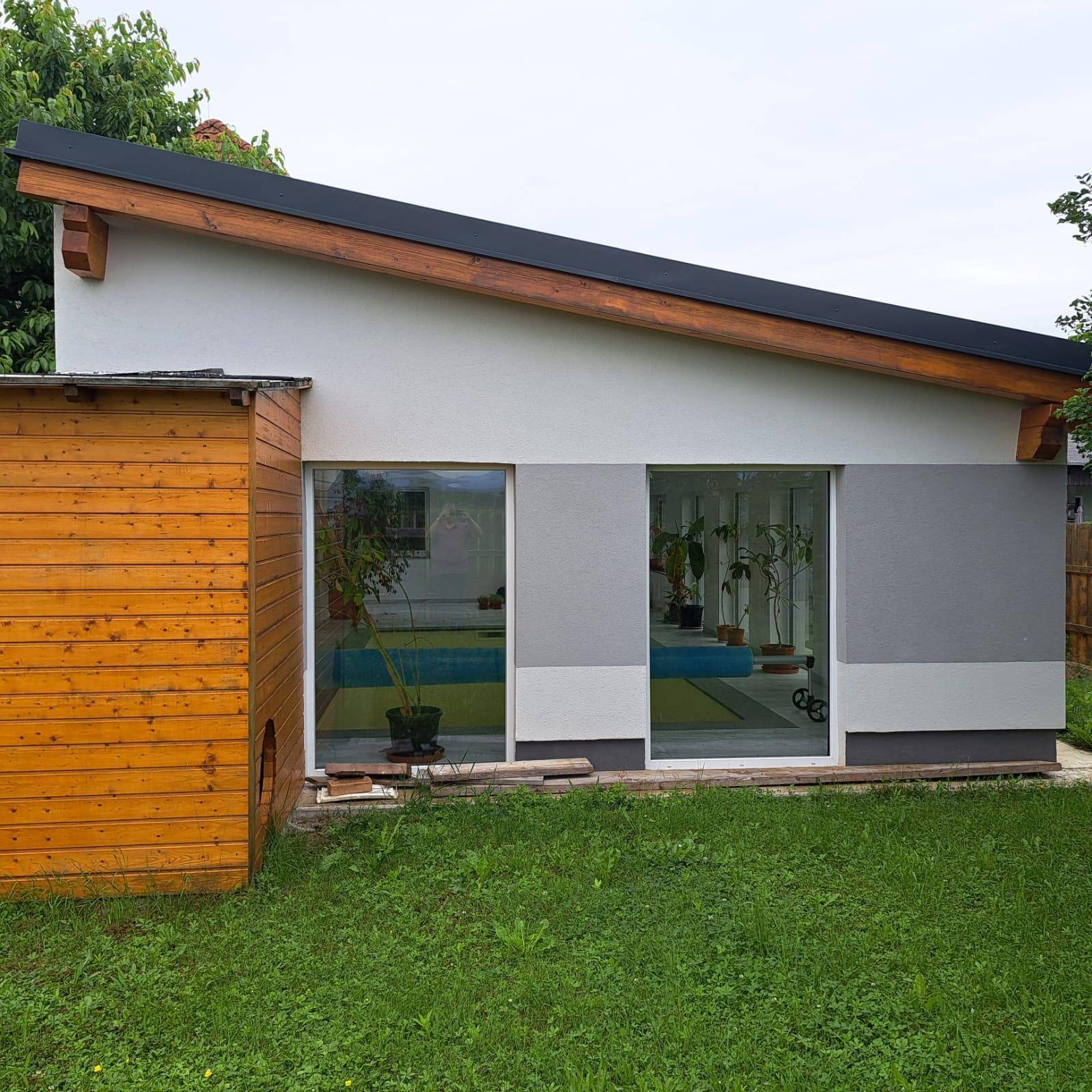 Seitenansicht des Hauses mit großen Fenstern zum Innenpool und angrenzendem Gartenbereich.