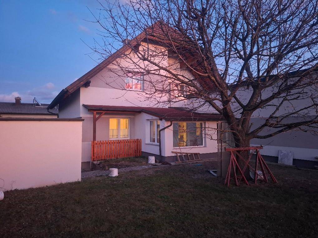 Rückseite des Hauses mit Garten, Schaukel und Bäumen bei Abenddämmerung.