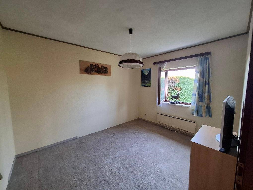 Schlichtes Schlafzimmer mit Teppichboden, Fensterblick ins Grüne und einfacher Einrichtung.