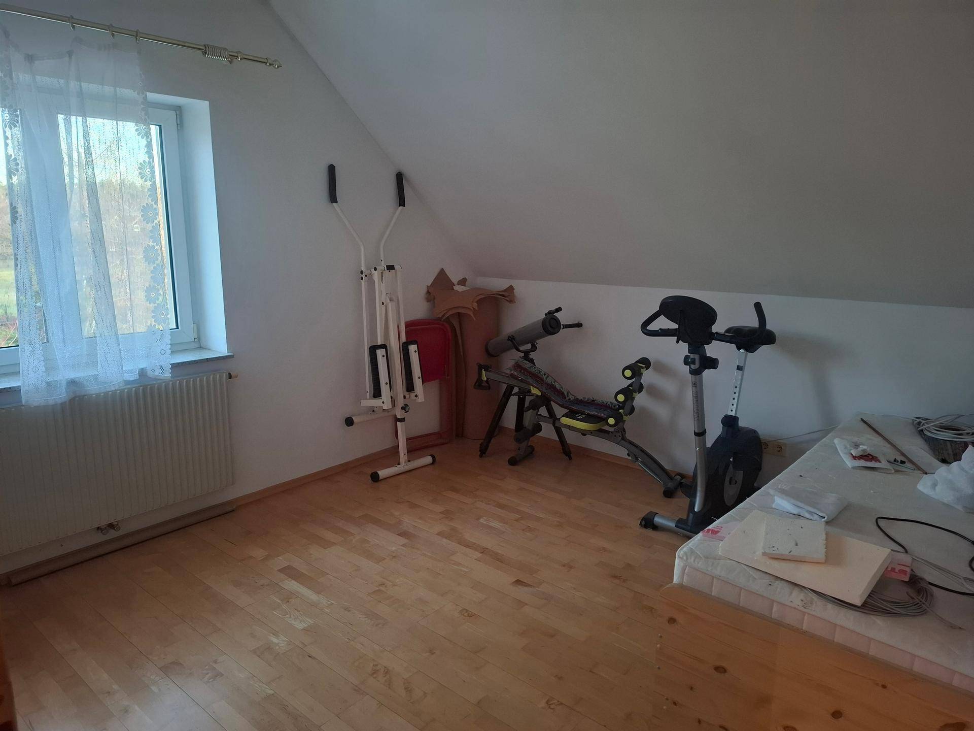 Heller Raum im Dachgeschoss, genutzt als Fitnessbereich mit Laminatboden und Fenster.