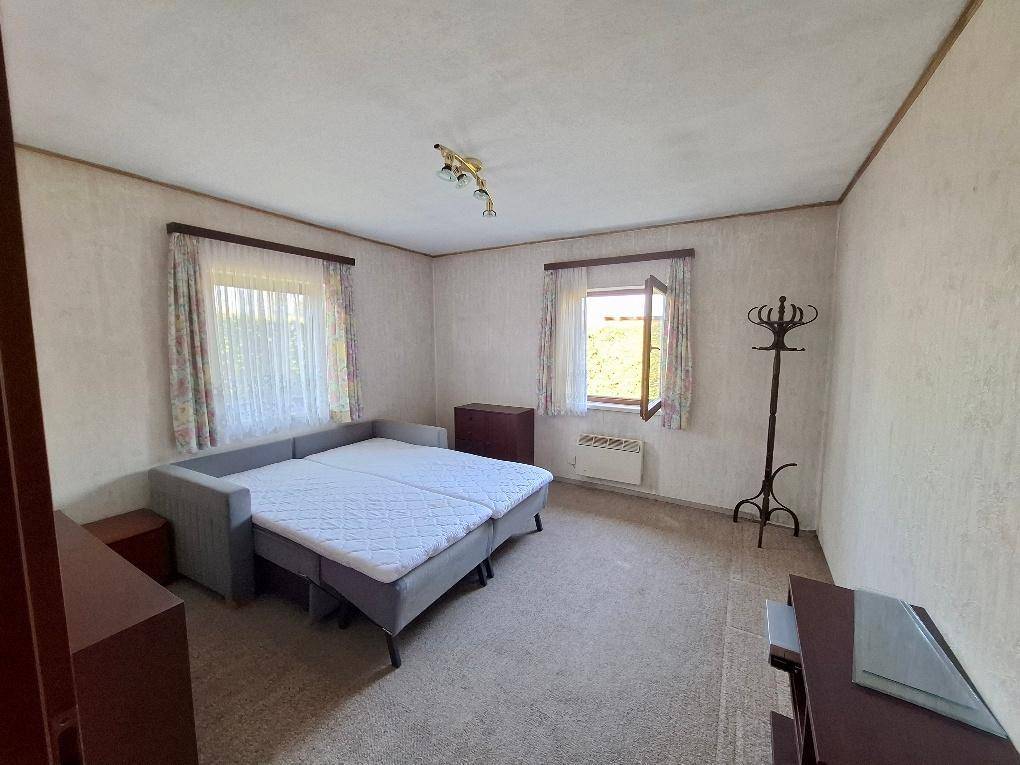 Helles Schlafzimmer mit Teppichboden, zwei Fenstern und einem Schlafsofa.