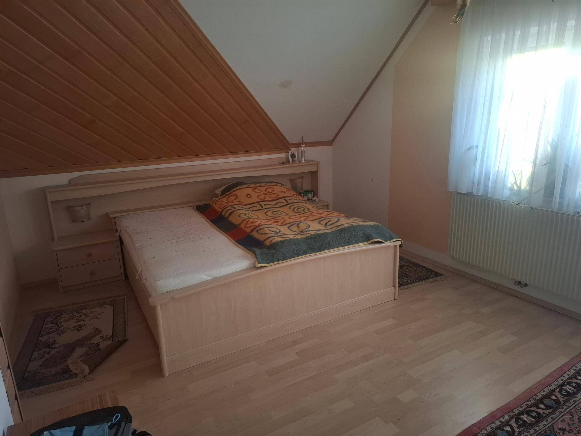 Schlafzimmer im Dachgeschoss mit Holzbett, Laminatboden und schräger Decke.