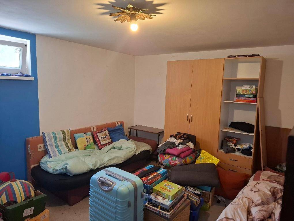 Zimmer im Untergeschoss mit Sofa, Kleiderschrank, Regal und einem kleinen Fenster für Tageslicht.