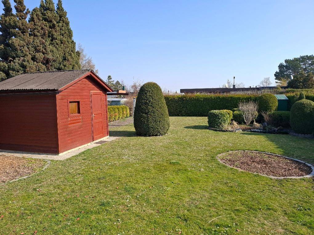 Großer, sonniger Garten mit Rasenfläche, hohen Hecken und einem roten Gartenhaus.