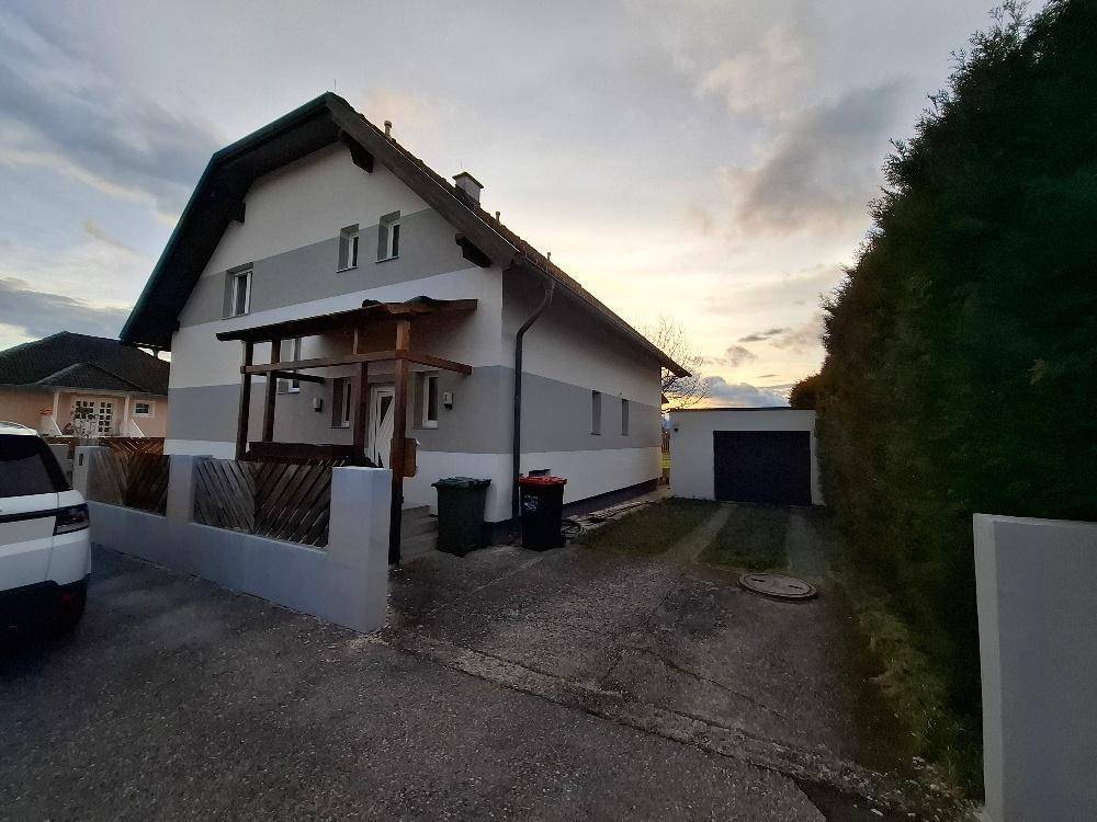 Rückseite des Hauses mit Einfahrt zur Garage und gepflegtem Gartenbereich bei Sonnenuntergang.
