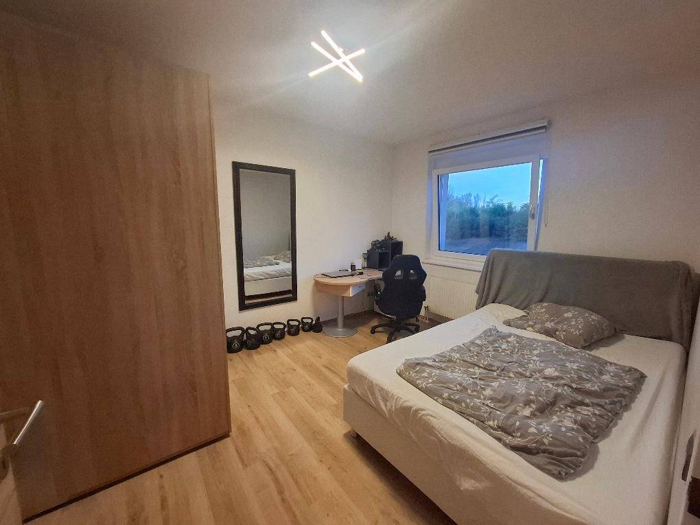 Schlafzimmer mit Einzelbett, großem Kleiderschrank, Schreibtisch und einem Spiegel auf Holzfußboden.