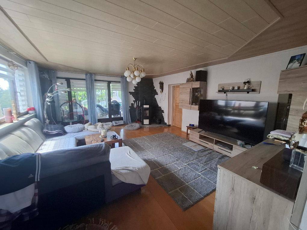 Helles Wohnzimmer mit Kaminofen, großem Fernseher und Zugang zur Terrasse.