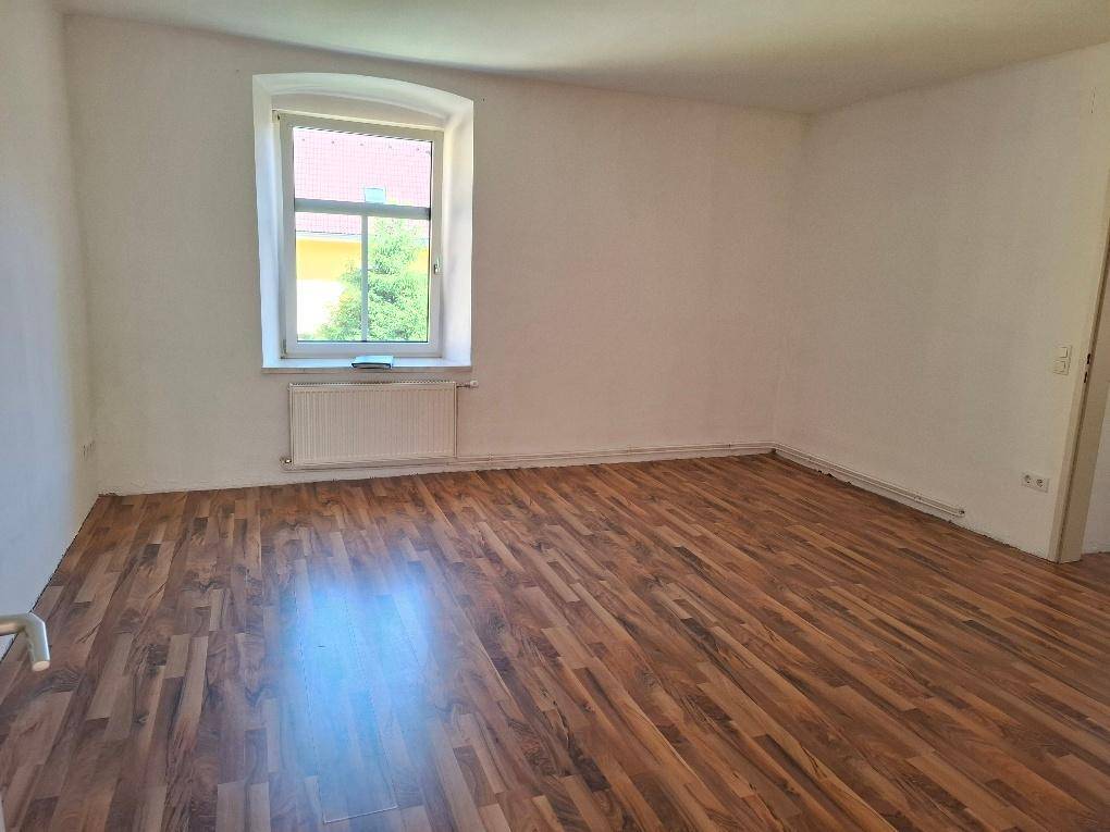 Geräumiges Zimmer mit Laminatboden, großem Fenster und Blick ins Grüne.