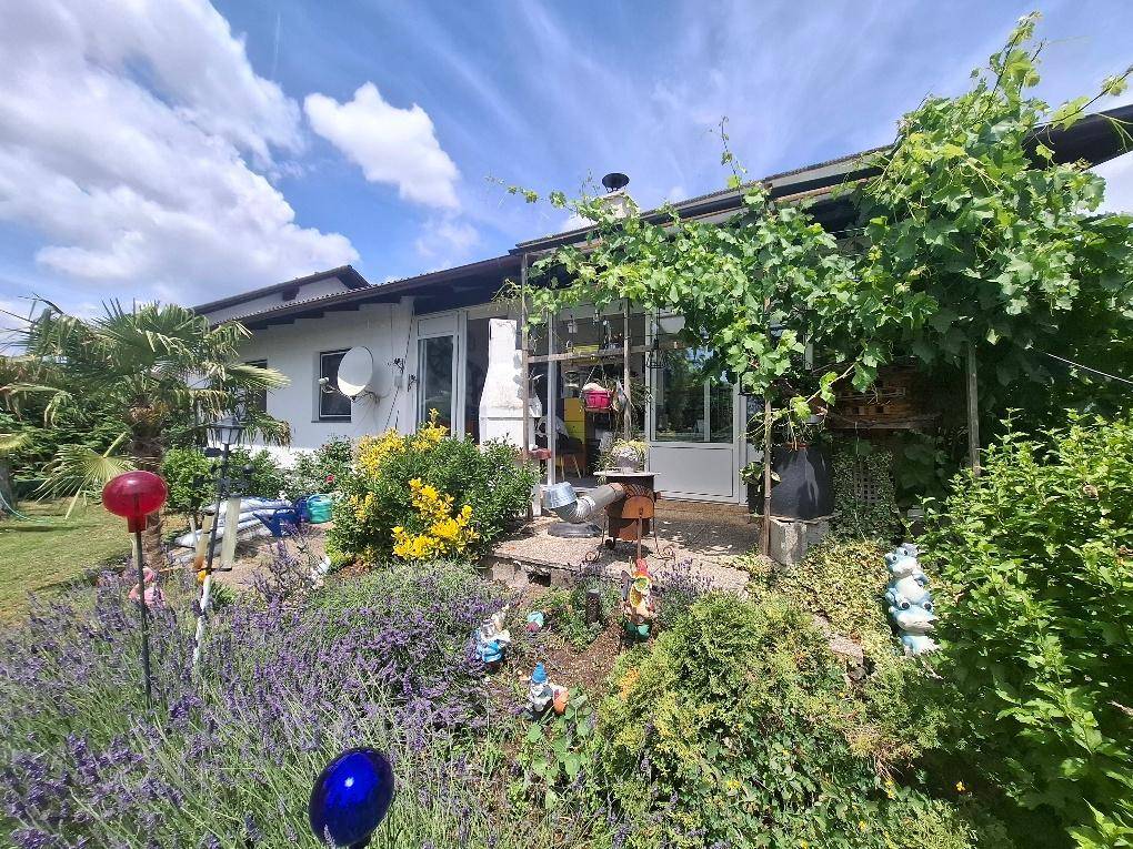 Rückseite des Hauses mit einem blühenden Garten, überdachter Terrasse und Gartenzwergen.