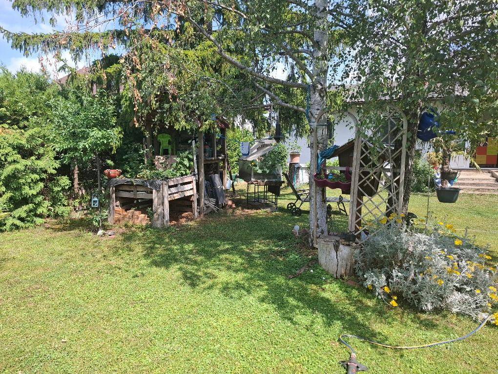 Teil des Gartens mit schattigen Bäumen, Holzstrukturen und üppiger Vegetation.