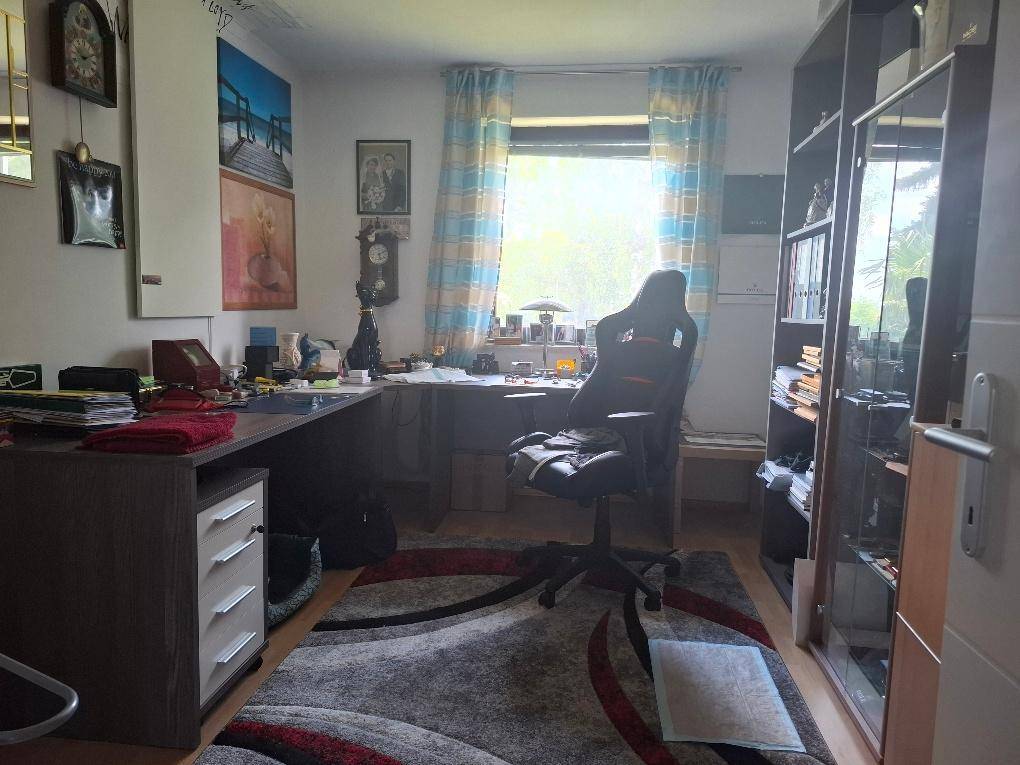 Arbeitszimmer mit großem Schreibtisch, Bücherregal und Teppichboden.