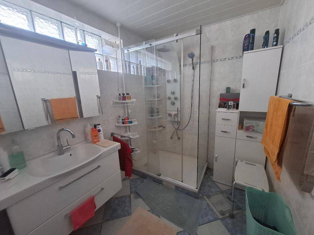 Modernes Badezimmer mit Duschkabine, Waschtisch und hellen Fliesen.