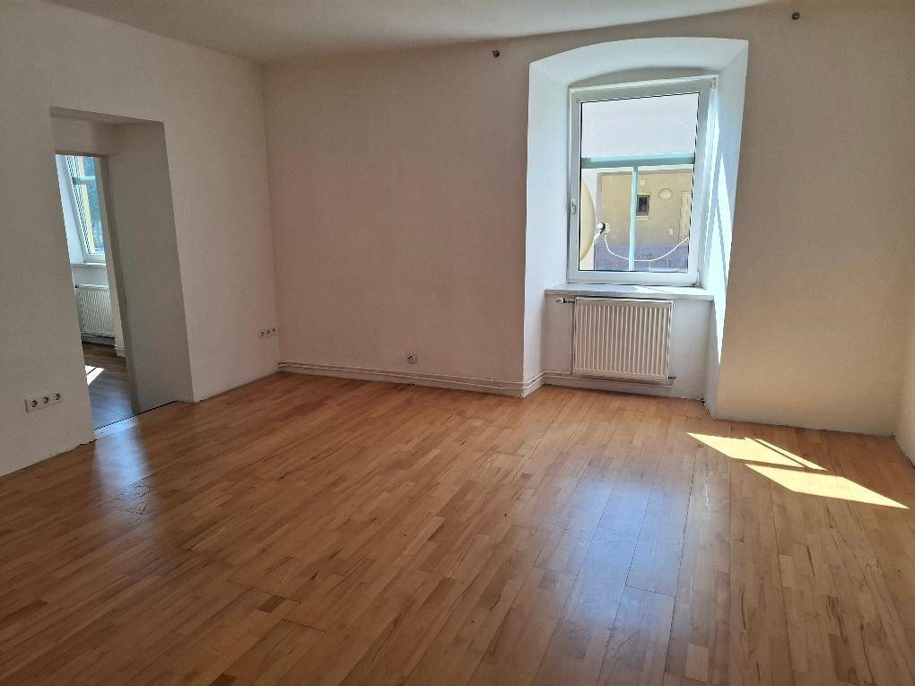 Lichtdurchflutetes Zimmer mit Laminatboden, Heizkörper und einem Fenster mit Rundbogen.