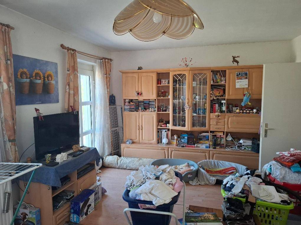 Wohnzimmer mit großem Holzschrank, Fenster und einem Deckenventilator, der viel Licht hereinlässt.