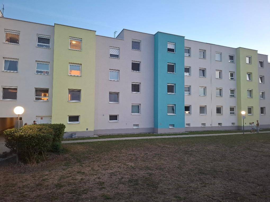 Mehrstöckiges Wohngebäude mit einer farbenfrohen Fassade in Grau, Hellgrün und Blau, umgeben von einer Rasenfläche.